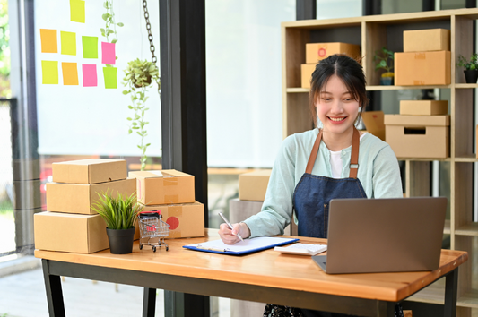 A woman smiling as she uses her laptop to manage her ecommerce business which is flourishing from the benefits of printed mailing materials